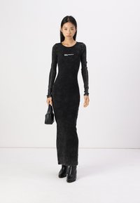 Svart långärmad åtsittande klänning i ett mjukt, strukturerat tyg med rund halsringning och logotypdetalj, i kombination med svarta accessoarer.