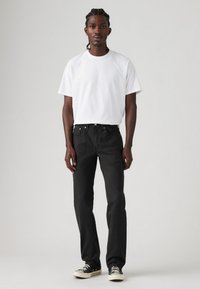 Zwarte jeans met een rechte snit, gecombineerd met een eenvoudig wit T-shirt met korte mouwen; gedragen met zwart-witte canvas sneakers.
