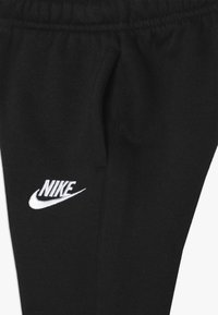 Pantalones deportivos negros con cintura elástica, que presentan un logo de Nike blanco bordado en la parte inferior de la pierna. Textura de tela suave y lisa.