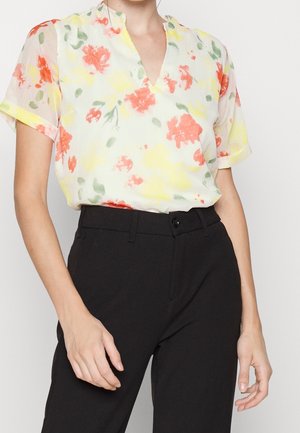 Blusa floreale in tessuto morbido e leggero, con un motivo di fiori gialli, verdi e rossi su uno sfondo chiaro. Collo a V e maniche corte.