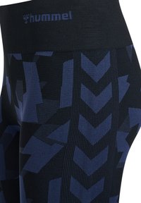 Marinblå leggings med ett brett midjeband som har en subtil houndstooth- och zigzag-design, tillverkade av ett elastiskt textilmaterial.