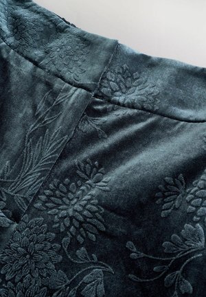 Dark teal velvet fabric featuring an embossed floral pattern. The surface has a soft texture with delicate detailing and a smooth finish.