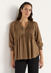 Brun, langærmet bluse med V-hals og plisseret design. Har samlet detalje ved brystet og elastiske manchetter. Glat tekstur.