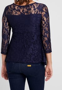 Mörkblåspetsblus med trekvartslånga ärmar, med blommönster och peplumskärning, i kombination med mörka denimjeans.