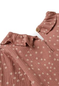 Tessuto rosa testurizzato con pois bianchi, dotato di un colletto arricciato e un'opzione di chiusura a bottone vicino al collo.