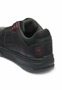 Sneaker nera in pelle con dettagli in rete, accenti bordeaux, design perforato e suola in gomma. Presenta una stampa del logo sul tallone.