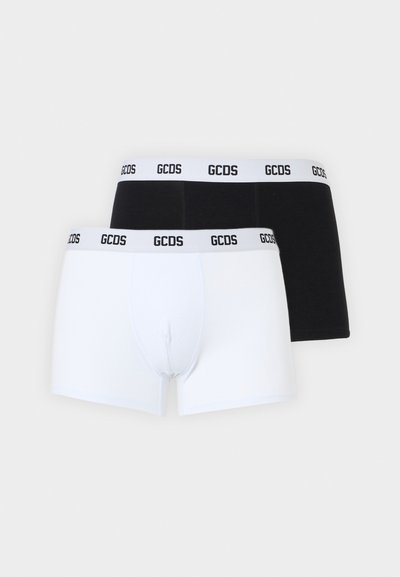 Deux paires de boxers pour hommes, une blanche et une noire, toutes deux avec des tailles élastiques blanches portant l'inscription "GCDS" en texte noir.