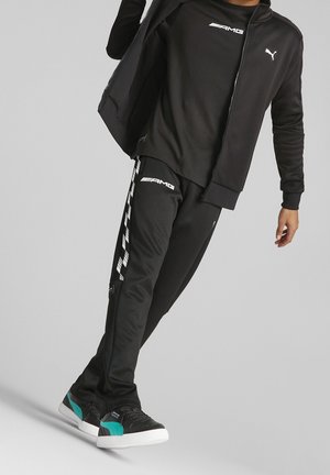 Osoba nosící černou bundu Puma, černé tričko AMG, černé tepláky AMG s bílými pruhy a černé tenisky s tyrkysovými akcenty.