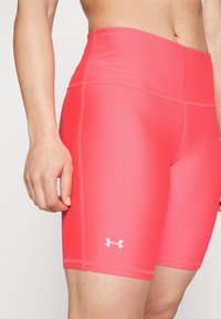 Rosa högmidjade träningsshorts gjorda av slätt, stretchigt material med platta sömmar och en liten vit logotyp på nedre benet.