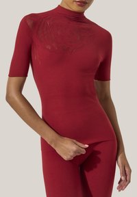 Röd figurnära topp med korta ärmar och hög hals, med ett strukturerat ros-mönster på vänster axel. Slät, elasticitet i tyget.