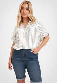 Valkoinen lyhythihainen pusero, jossa on pystysuorat mustat raidat ja V-pääntie. Yhdistetty korkeavyötäröisten tummansinisten farkkuhousujen kanssa, joiden lahkeet on käännetty.