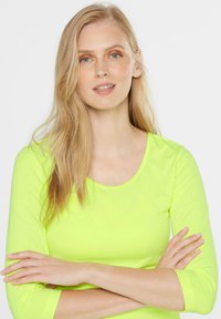 Neon-gelbes Langarmshirt mit rundem Ausschnitt und weicher Textur, ausgestattet mit Dreiviertelärmeln und enganliegendem Design.
