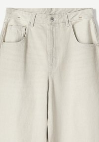 Pantalons en coton beige clair à taille haute, dotés de deux poches avant, d'une fermeture à bouton et de détails de couture contrastants.