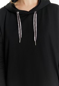 Fekete kapucnis hoodie, fékeresztbe szőtt fehér és fekete részletekkel, puha tapintással és laza szabással. Minimalista dizájn, minta nélkül.
