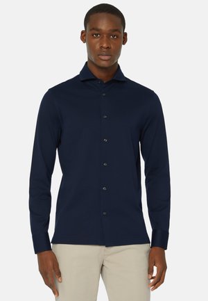 Navy long-sleeve shirt in soft fabric with a buttoned front, pointed collar, and fitted design. Features subtle texture and dark buttons.