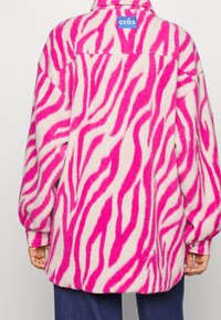 Rosa och vit randig fleecejacka med avslappnad passform, som har en blå etikett på baksidan och en mjuk textur.