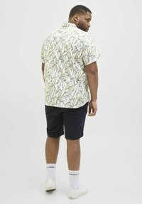 Camisa de manga corta blanca con un patrón de hojas en amarillo y azul; combinada con pantalones cortos azul marino y zapatillas blancas con calcetines hasta el tobillo.