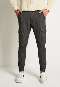 Koolgrijze cargobroek met elastische boorden, voorzien van zijzakken en een gestructureerde stof. Gecombineerd met witte sneakers voor contrast.