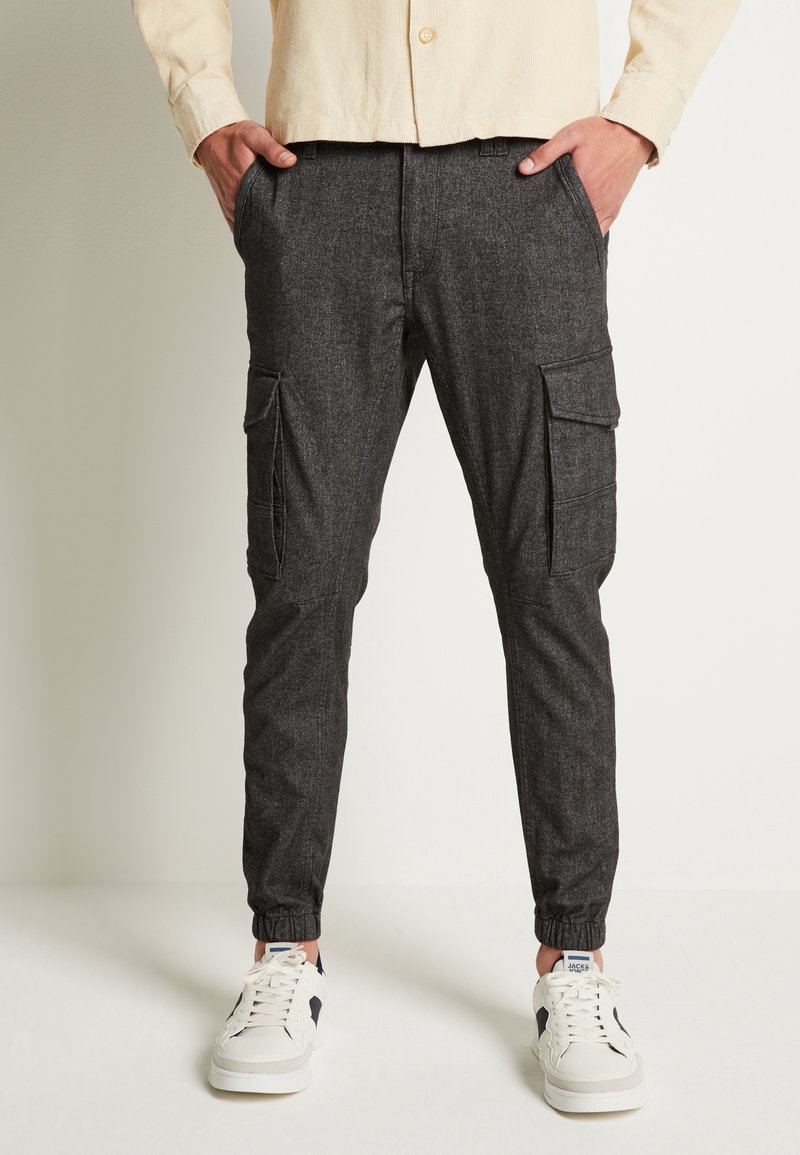 Koolgrijze cargobroek met elastische boorden, voorzien van zijzakken en een gestructureerde stof. Gecombineerd met witte sneakers voor contrast.