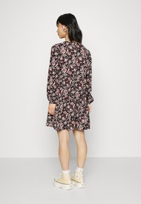 Vestido floral de mangas longas com fundo preto, apresentando flores rosa e brancas, com saia franzida e punhos elásticos. Usado com botas bege.