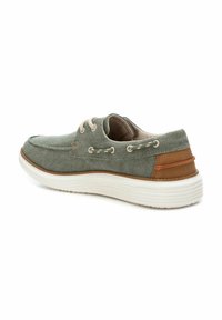 Zapatilla de tela gris con suela blanca, acentos en marrón en el talón, cordones beige y costuras decorativas en los laterales.