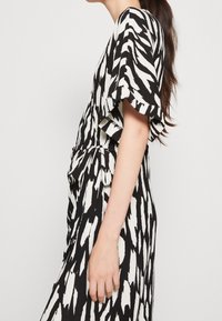 Vestido de patrón blanco y negro con mangas cortas de volante, cintura anudada y corte holgado, que presenta un tejido texturizado y un diseño drapeado.