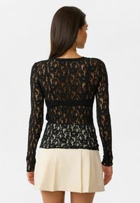 Zwarte kant lange mouwen top met een bloemenpatroon, transparante textuur en een getailleerd ontwerp, gecombineerd met een crèmekleurige rok.