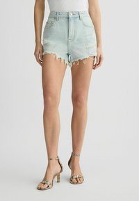 Pantalones cortos de mezclilla azul claro con dobladillos deshilachados y detalles desgastados, combinados con sandalias de tacón alto de estampado de serpiente con tiras finas.