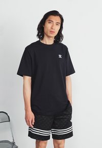 Čierne bavlnené tričko s okrúhlym výstrihom a malým logom, spojené s čiernymi šortkami s tónovým vzorom a bielymi pruhmi.