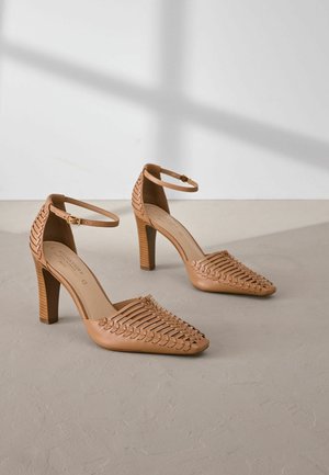 Pantofi cu toc înalt din piele maro, cu un design împletit în față, vârful ascuțit și bretelela la gleznă. Tocurile din lemn pătrat oferă stabilitate.