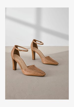 Hnědé kožené lodičky na vysokém podpatku s pleteným designem vpředu, špičatou špičkou a páskem kolem kotníku. Čtvercové dřevěné podpatky zajišťují stabilitu.