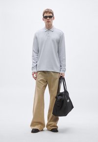 Ανοιχτό γκρι μακρυμάνικο πόλο πουκάμισο, χακί παντελόνι με φαρδιά μπατζάκια, μαύρα γυαλιά ηλίου και μαύρη τσάντα tote με λευκά γράμματα. Λείο υλικό, casual σχέδιο.