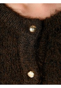Brun stickad kofta med en texturerad väv och en spiralformad knapp i guldton vid halsringningen för en funktionell detalj.