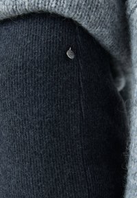 Pull en maille foncée avec une finition texturée, agrémenté d'un accent de ton argenté. L'encolure est gris clair et légèrement lâche sur les bords.