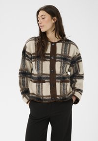 Flanell-Fleecejacke in Creme, Braun und Schwarz. Vorderseite mit Knöpfen, rundem Ausschnitt und Seitentaschen. Weiche Textur mit entspannter Passform.