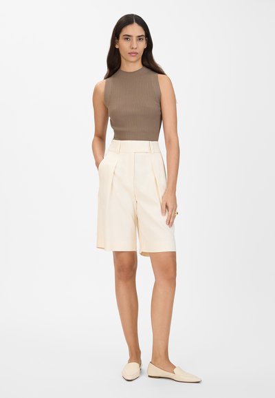 Un haut sans manches en rib côtelé marron associé à un short crème taille haute avec des plis avant et des poches latérales. Accentué par des chaussures beiges plates.