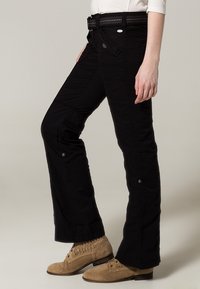 Pantalons en coton noirs à coupe droite, dotés de poches avant, de boutons et d'une ceinture noire texturée. Portés avec des bottines beige clair.