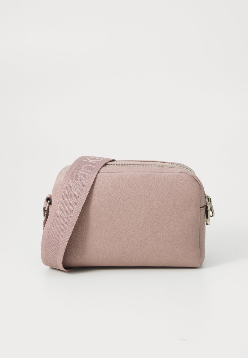 Geantă crossbody din piele roz, cu închidere cu fermoar și o curea împletită, având logo-ul "Calvin Klein". Formă compactă, rectangulară, cu finisaj texturat.