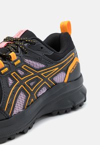 Black athletic shoe with orange accents, textured mesh panels, and a rugged sole. Lace-up design with a pull tab at the heel.