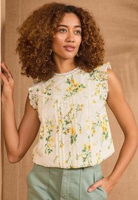 Blusa senza maniche floreale bianca con motivi gialli e verdi, dotata di maniche arricciate e collo rifinito in pizzo. Tessuto testurizzato.