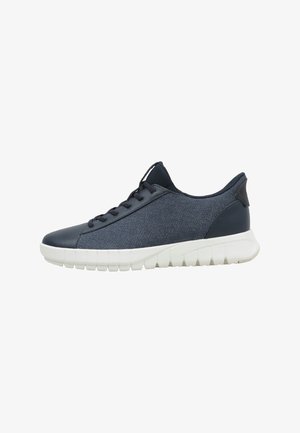 Zapatilla baja azul oscuro con parte superior de tela y cuero, cordones negros y suela gruesa de goma blanca con ranuras profundas.