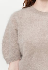 Svijetlosmeđi kratkotrajni pulover s kratkim rukavima, napravljen od mekog, pahuljastog materijala, s okruglim izrezom i rebrastim detaljima na rubovima.