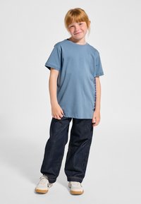 Ljusblå bomullst-shirt med korta ärmar och rak skärning, kombinerad med mörkblå denimjeans och vita sneakers med beige detaljer.