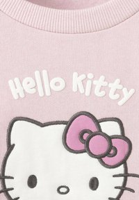 Hanorac roz deschis cu fața brodată Hello Kitty, având o fundiță roz și inscripția albă "Hello Kitty". Textură moale a materialului.