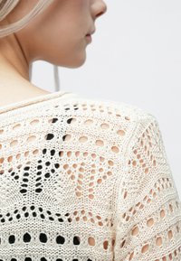 Maglione lavorato a maglia color crema con motivo a intaglio e accenti neri a contrasto, caratterizzato da un collo rotondo e maniche corte.