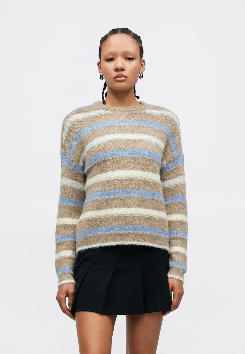 Stripete genser med myk, lodden tekstur; fargene inkluderer beige, krem og blå. Har rund hals og lange ermer.