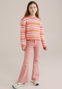 Pulover tricotat în dungi în nuanțe de roz și portocaliu, asortat cu pantaloni evazați de un roz deschis și adidași albi cu accente multicolore.
