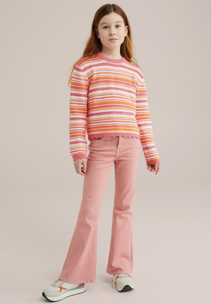 Pulover tricotat în dungi în nuanțe de roz și portocaliu, asortat cu pantaloni evazați de un roz deschis și adidași albi cu accente multicolore.
