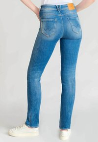 Jean en denim bleu skinny avec un lavage délavé, comprenant deux poches arrière avec une couture en zigzag et une étiquette de marque à la taille.