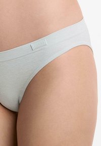 Svijetlosivi pamučni tangice s glatkom teksturom. Ima široku elastičnu gumicu s malom oznakom branda. Minimalistički dizajn.